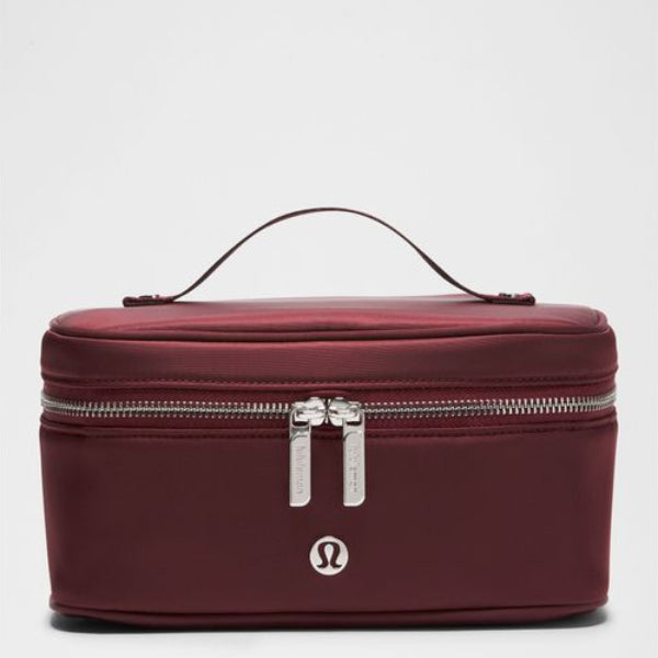 A rectangular, deep burgundy cosmetic bag with a top handle, silver zippers, and a silver Lululemon logo on the front, set against a light gray background.
